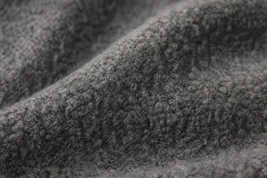 Close-up of a dark gray textured fabric with a looped or boucle-like surface, filling the frame.