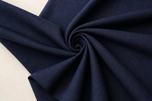 A close-up of dark navy blue fabric arranged in a spiral drape against a light off-white background.