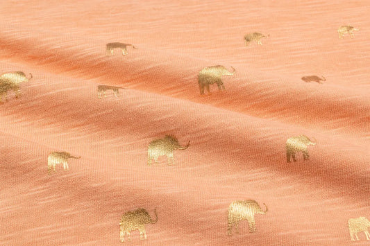 A close-up of peach-colored fabric with a repeating pattern of small metallic gold elephants.