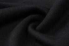 A close-up of black ribbed knit fabric with soft folds and a smooth texture.