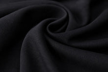 A close-up of draped black fabric with soft folds and a fine ribbed texture.