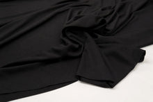 Black fabric draped and folded on a white surface, showing a smooth texture and soft folds.