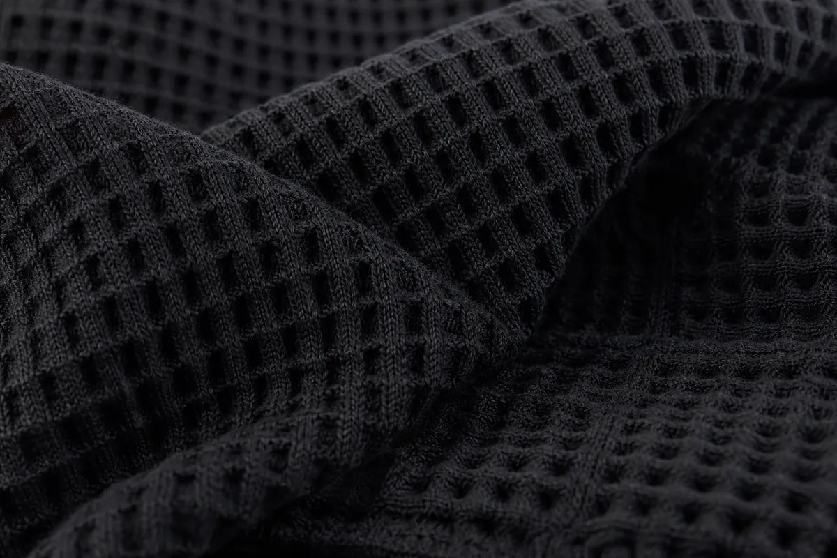 Close-up of a dark charcoal gray waffle knit fabric with a textured grid pattern, draped in soft folds.