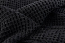 Close-up of a dark charcoal gray waffle knit fabric with a textured grid pattern, draped in soft folds.