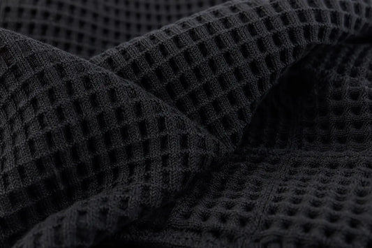 Close-up of a dark charcoal gray waffle knit fabric with a textured grid pattern, draped in soft folds.