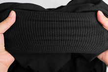 Close-up of a black ribbed knit fabric being held stretched by two hands to show its texture and elasticity.