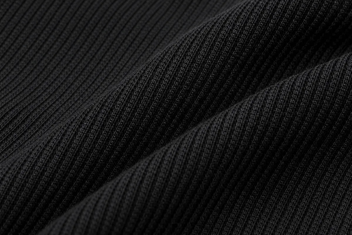 Close-up of a black ribbed knit fabric with soft diagonal folds showing the texture and weave.