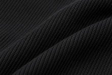 Close-up of a black ribbed knit fabric with soft diagonal folds showing the texture and weave.