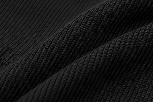Close-up of a black ribbed knit fabric with soft diagonal folds showing the texture and weave.