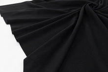 Black ribbed knit fabric draped in soft folds against a plain white background.