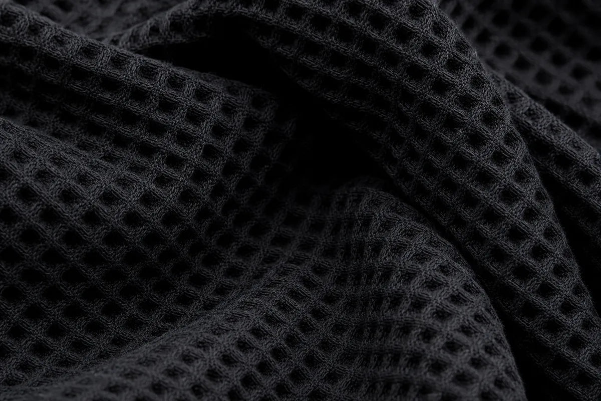 Close-up of a black waffle-knit fabric with a textured grid pattern and soft folds.