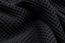 Close-up of a black waffle-knit fabric with a textured grid pattern and soft folds.