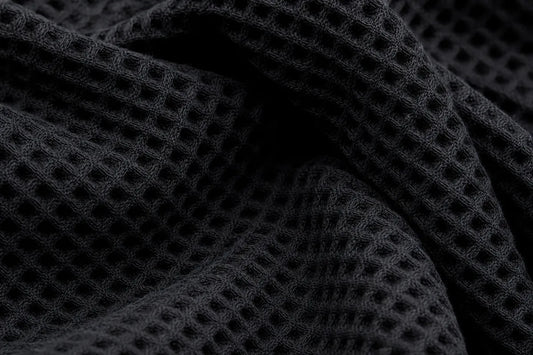 Close-up of a black waffle-knit fabric with a textured grid pattern and soft folds.