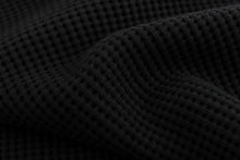 Close-up of a black waffle-knit fabric with a textured grid pattern and soft folds.
