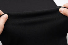 Close-up of a person's hands stretching a black ribbed knit fabric to show its elasticity and texture.