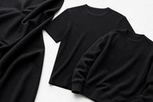 Two black crewneck knit tops, one short-sleeve and one long-sleeve, arranged on a white background with a draped black fabric piece on the left.