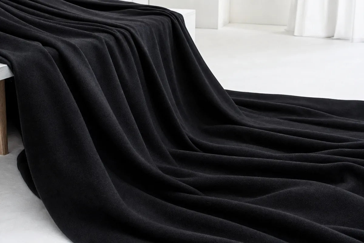 A thick, plush black throw blanket draped elegantly over a white bench in a minimalist, bright room.