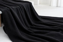 A thick, plush black throw blanket draped elegantly over a white bench in a minimalist, bright room.