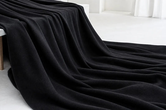 A thick, plush black throw blanket draped elegantly over a white bench in a minimalist, bright room.