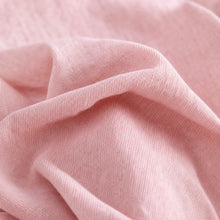 A close-up of soft pink fabric with gentle folds and a fine woven texture.
