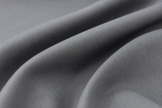 A close-up of draped gray fabric with a fine ribbed texture, showing soft folds and shadows.