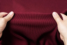 Close-up of a person's hands stretching a deep burgundy ribbed knit fabric to show its elasticity.