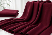 A deep burgundy ribbed knit throw blanket draped elegantly on a white surface, with a folded matching blanket in the background.