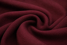 A close-up of dark burgundy ribbed knit fabric, swirled into elegant folds to show off its texture and drape.