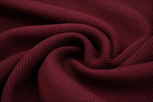 A close-up of dark burgundy ribbed knit fabric, swirled into elegant folds to show off its texture and drape.