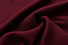 A close-up of draped ribbed fabric in a deep burgundy red color, showing the texture and folds.
