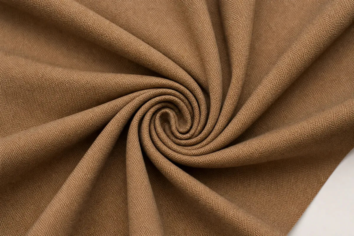 A close-up of draped brown fabric arranged in a spiral pattern, showing its texture and color against a small white corner in the bottom right.