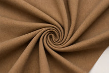 A close-up of draped brown fabric arranged in a spiral pattern, showing its texture and color against a small white corner in the bottom right.
