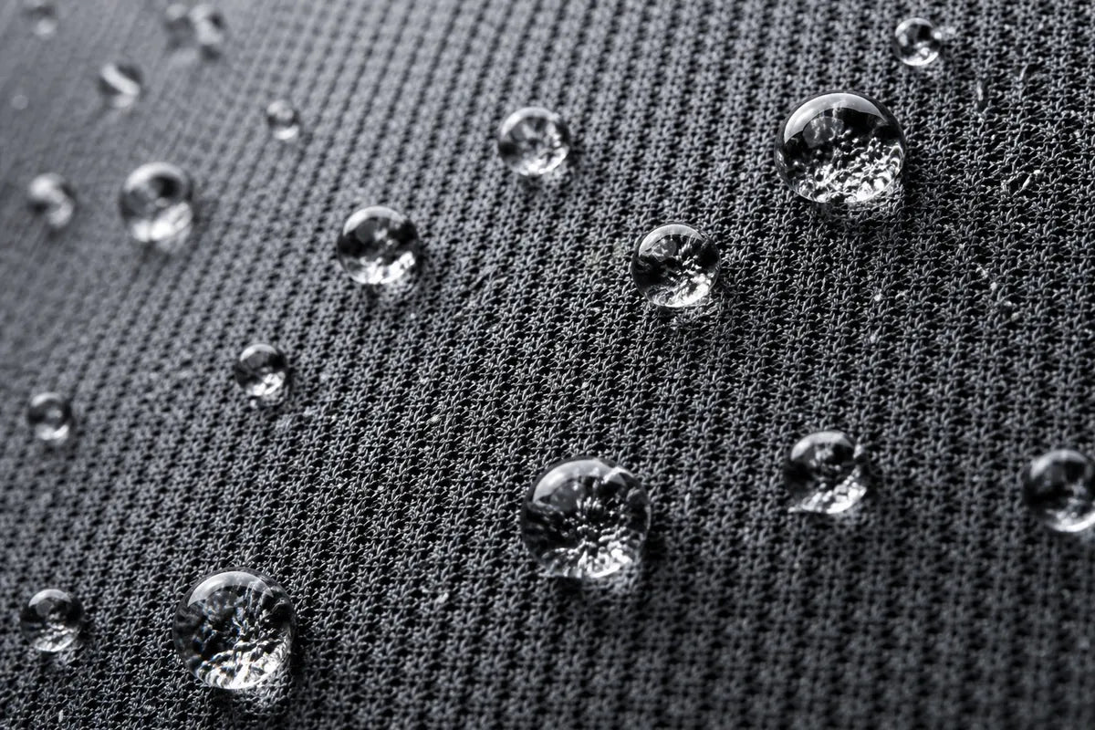 Close-up of clear water droplets resting on a dark textured fabric surface.