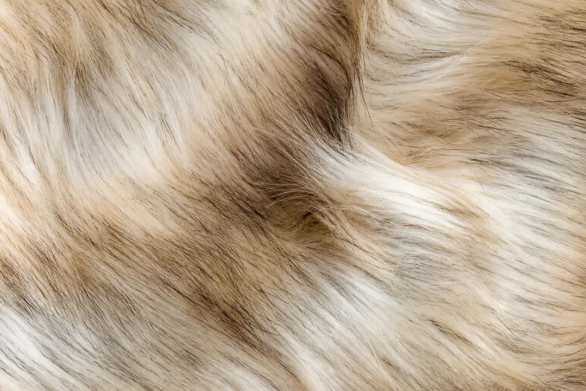 A close-up texture shot of shaggy faux fur fabric in a mottled blend of beige, cream, and light brown tones.