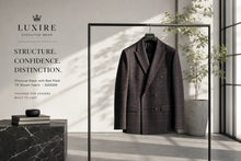 A charcoal black double-breasted blazer with a subtle red plaid pattern hangs on a black clothing rack in a modern interior setting. The brand name 'LUXIRE EXECUTIVE WEAR' is displayed on the left side of the image with promotional text.