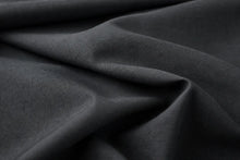 A close-up of draped dark charcoal gray fabric with soft folds and a fine woven texture.