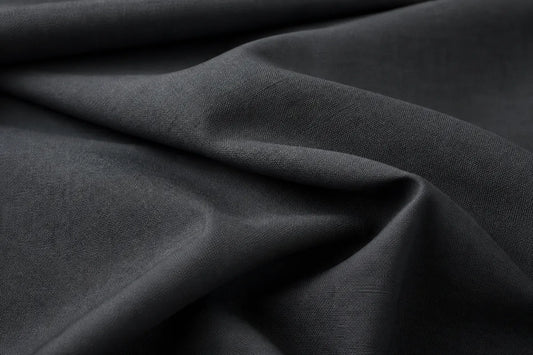 A close-up of draped dark charcoal gray fabric with soft folds and a fine woven texture.