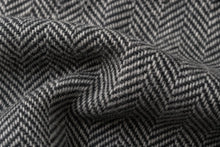 Close-up of a gray and white herringbone woven fabric with a textured chevron pattern, shown in soft folds.