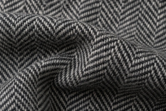 Close-up of a gray and white herringbone woven fabric with a textured chevron pattern, shown in soft folds.