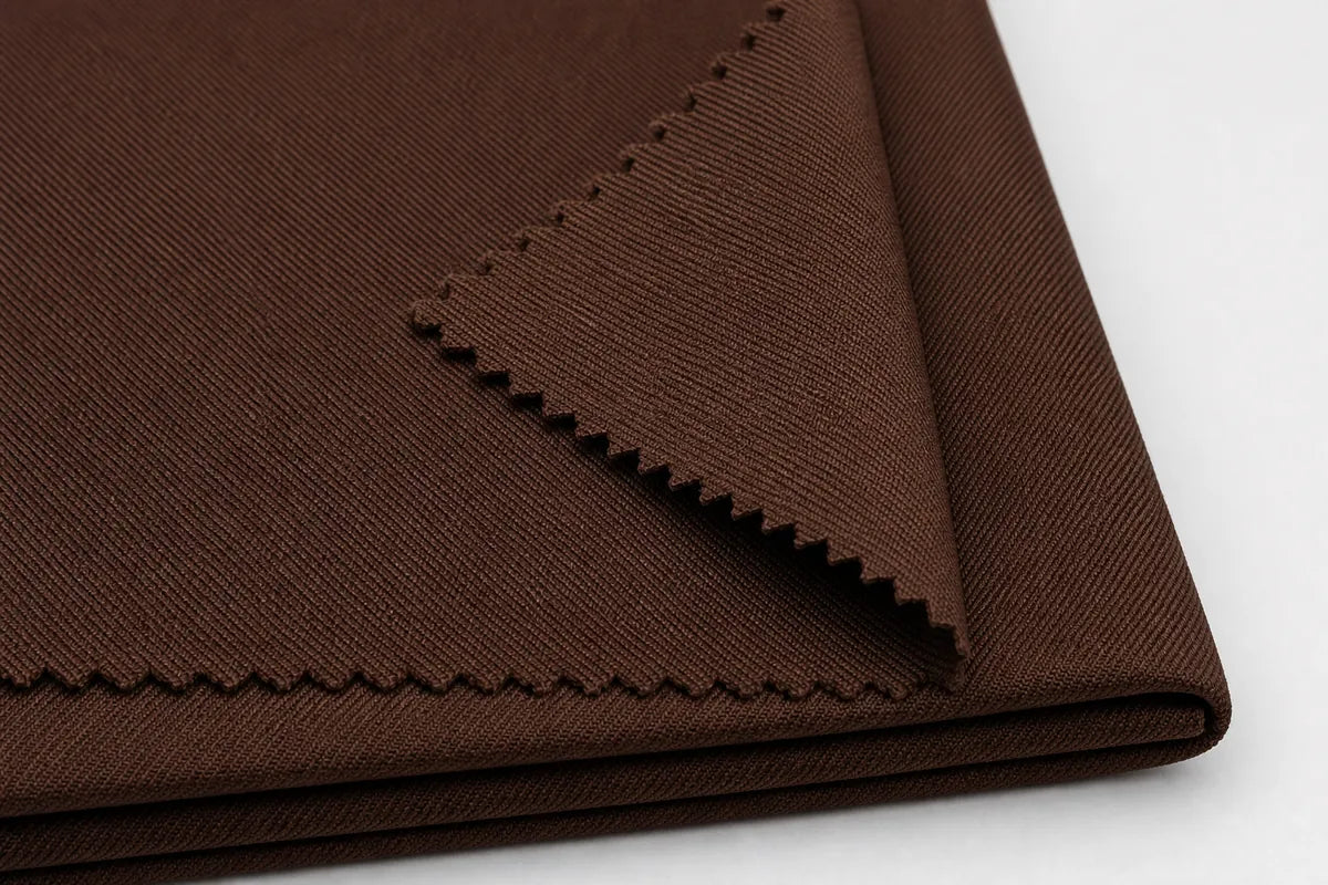A close-up of folded brown fabric with visible woven texture and zigzag-cut edges, photographed on a white background.