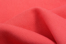 A close-up of textured coral pink knit fabric with soft folds showing the ribbed pattern.
