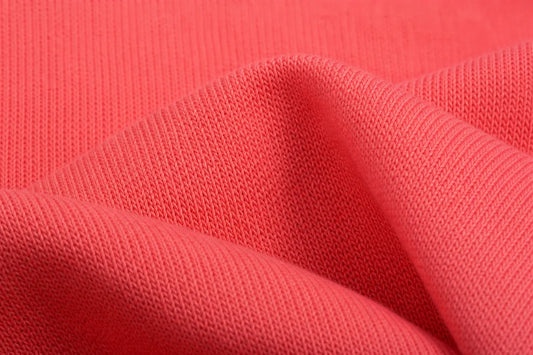 A close-up of textured coral pink knit fabric with soft folds showing the ribbed pattern.