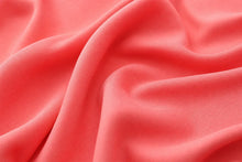 A close-up of draped coral pink fabric with soft folds and a smooth texture.