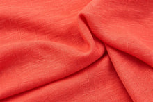 A close-up of draped coral pink fabric with a visible woven texture and soft folds.