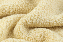 A close-up of a soft, textured cream or beige fleece fabric with a looped terry-like surface, shown in gentle folds.