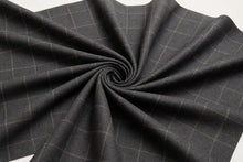 Dark gray windowpane plaid fabric draped in a spiral pattern, showing its texture and weave on a white background.