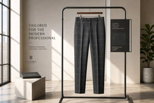 A pair of tailored dark gray plaid trousers hangs on a black clothing rack in a styled interior setting with warm sunlight, a plant, and branded Luxora booklets.