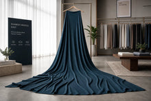 A long, dark teal-blue knit blanket or throw draped over a wooden hanger in a modern, stylishly decorated room. A black sign on the left reads 'BAMBOO WHATELL KNIT'.