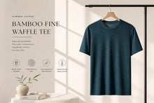 A dark teal bamboo fine waffle t-shirt hanging on a wooden hanger against a warm beige wall with soft window shadows. The left side of the image features promotional text reading 'BAMBOO FINE WAFFLE TEE' with icons for bamboo, fine waffle knit, lightweight, and temperature regulation.