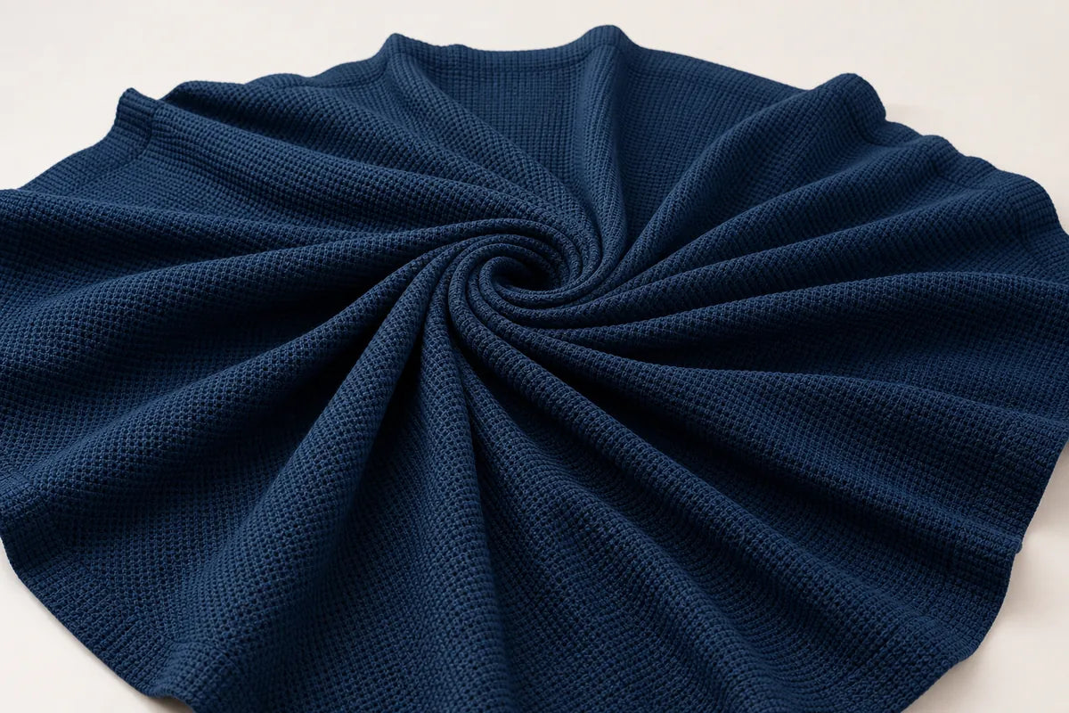 A dark navy blue textured fabric, likely a waffle-knit blanket or throw, arranged in a spiral pattern on a plain white background.